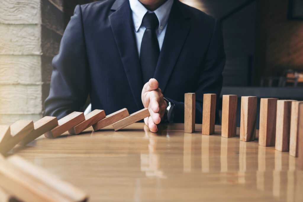 Close up of businessman hand stopping falling wooden dominoes