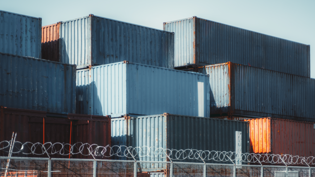 Stacked metal shipping containers stored behind a barbed-wire fence
